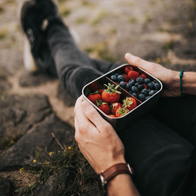 Hand hält Edelstahl-Lunchbox mit Beeren und Erdbeeren im Inneren