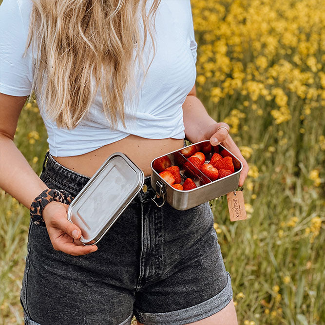 Edelstahl-Lunchbox mit Klappdeckel, gefüllt mit Erdbeeren; Person trägt sie