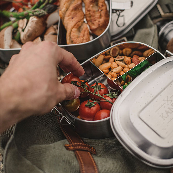 Offene Edelstahl-Lunchbox mit Gemüse, drei Fächer; Deckel liegt daneben