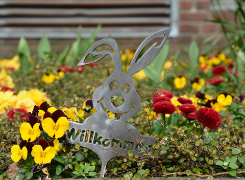 Kleiner Gartenstecker mit silbernem Hasen und „Willkommen“, zentriert im Blumenbeet