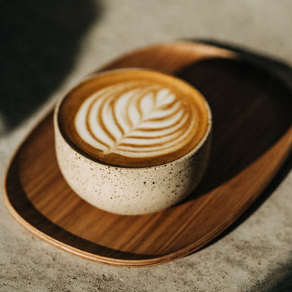 Cappuccino-Tasse mit Latte-Art-Muster im Schaum auf rundem Holztablett