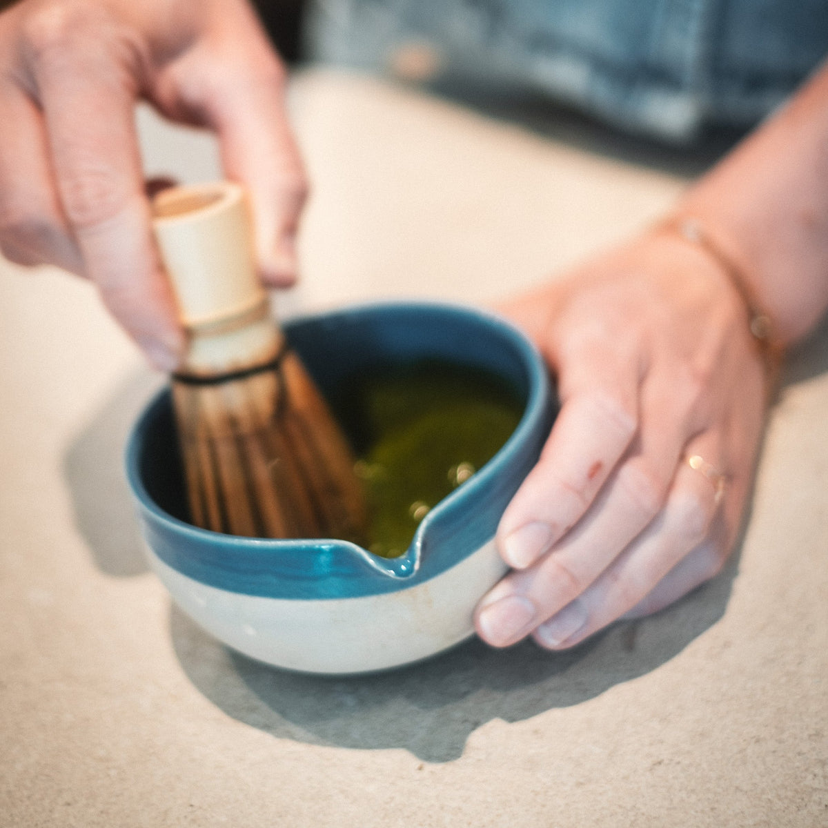 Blaues Matcha-Schälchen mit weißem Rand und Bambusbesen, Person hält Schale