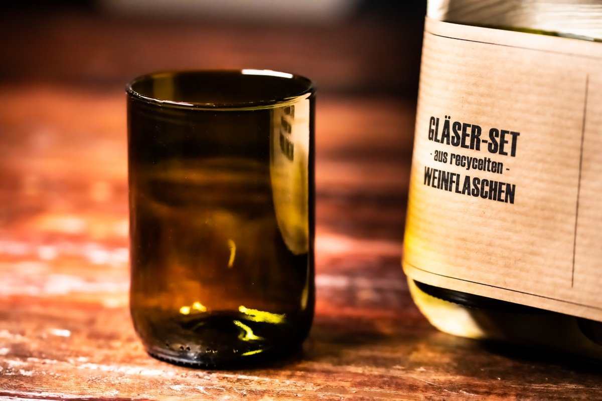 Dunkles Trinkglas aus Flaschenglas neben Kartonverpackung des Glas-Sets