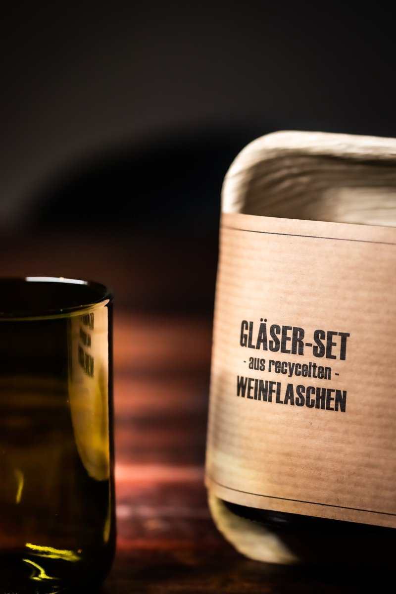 Trinkglas-Set: Kartonrolle und ein dunkler Glasbecher aus Flaschenglas
